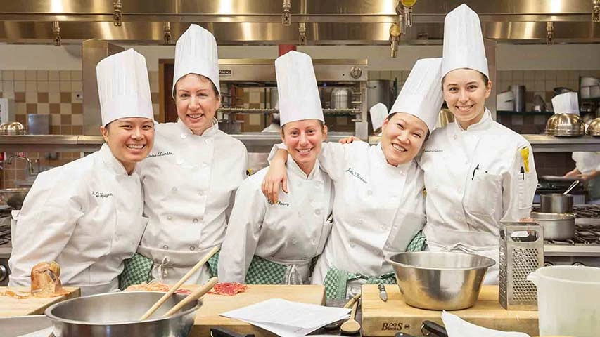 Smiling Culinary Institute of America students in the kitchen.